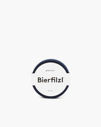 A set of circular dark-colored Merino wool coasters, wrapped in a white band labeled Bierfilzl by graf lantz, made in the USA. Background is plain white.