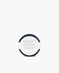 A graf lantz round container with a side view against a plain background showcases a white label with text. Its minimalist design, resembling Merino wool coasters, features a concise description on the label.