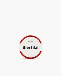 A round red felt coaster made from German Merino wool by graf lantz. It has a clean white label in the center with Bierfilzl in bold, accompanied by smaller text above and below, all set against a stark white background for a minimalist design.
