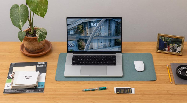 A gray felt tissue box and a wooden tray with a lipstick, perfume, and pen sit on a light wooden surface, with a mirror and tiled wall in the background.