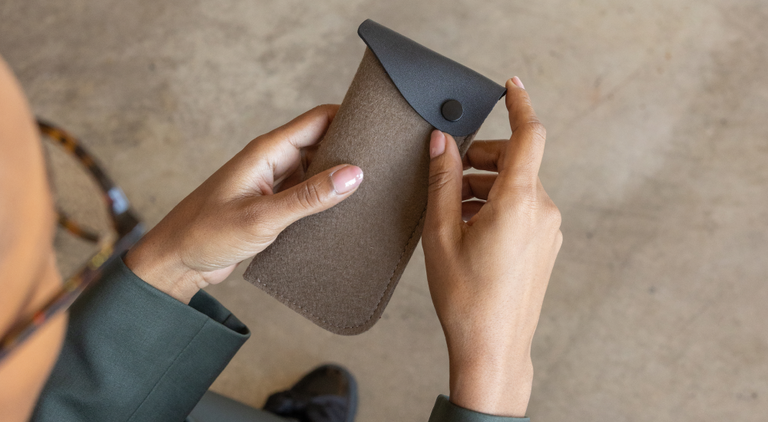 Two green felt eyeglass cases with brown leather trim sit on a wooden surface. One case is open, revealing a pair of glasses inside.