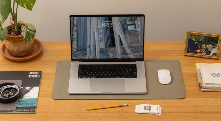 A laptop displaying 6:33 sits on a wooden desk with a mouse, pencil, plant, framed photo, books, notepad, and charging cables neatly arranged around it.