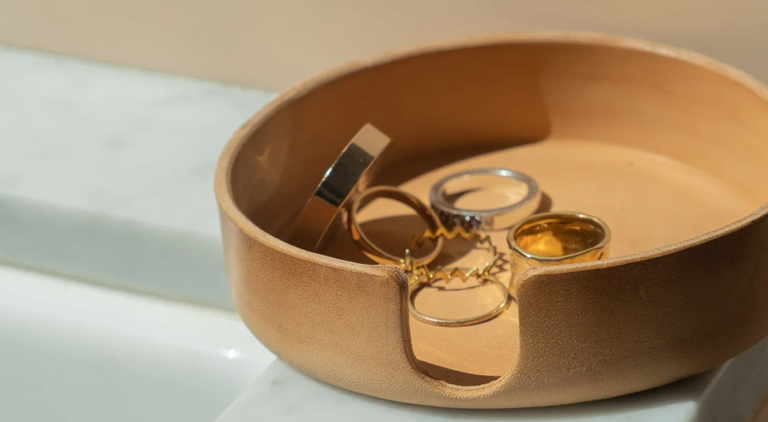 Two trays on a light surface hold office supplies: pens, pencils, clips, eraser, scissors, eyeglasses, a notebook, AirPods case, clear push pins, and a pack of chewing gum.
