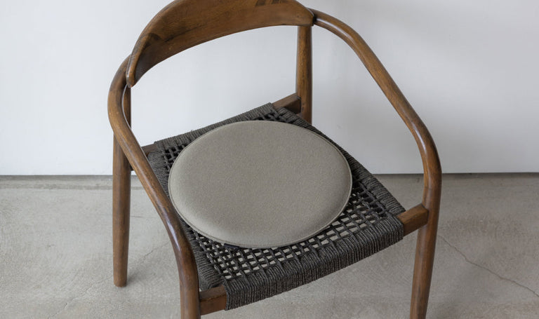 Green chair with a gray felt seat cushion, placed against a light striped wall.