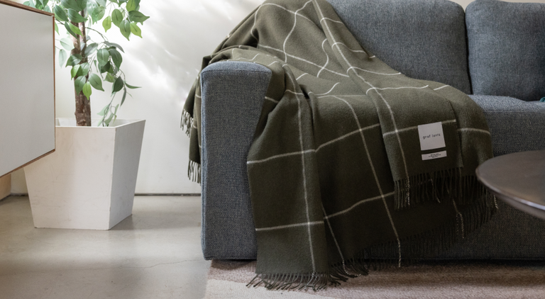 A person in a flowing white dress poses against a rocky background, holding out a long, sheer fabric that drapes elegantly behind them.