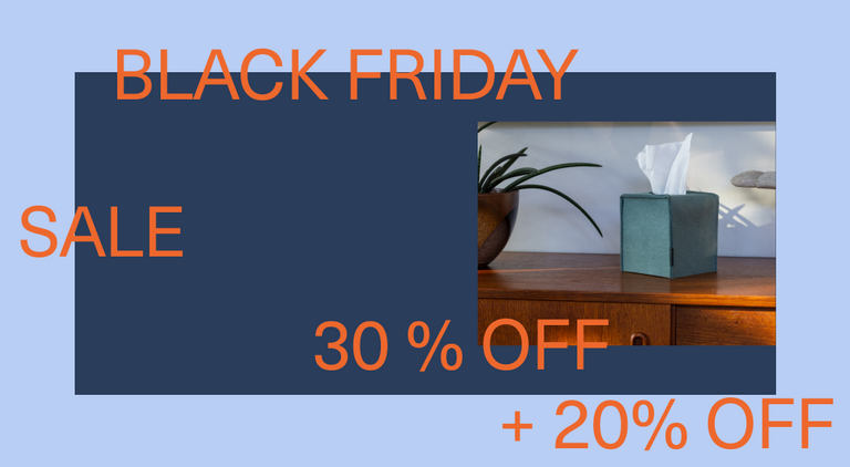 A person in a blue shirt reaches for a tissue from a square, brown tissue box on a wooden table. A guitar and a draped blanket are visible in the background, suggesting a cozy home setting.