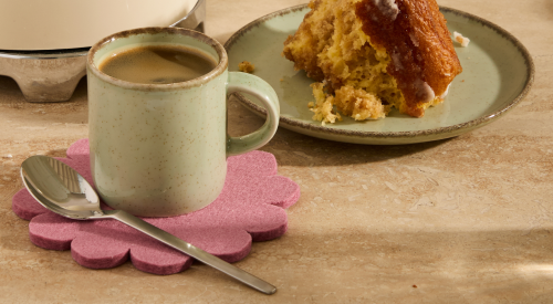 A person wearing a denim outfit sits in a comfortable chair by a window, wrapped in a soft pink blanket, holding an open book. The scene suggests a cozy, relaxed moment indoors.