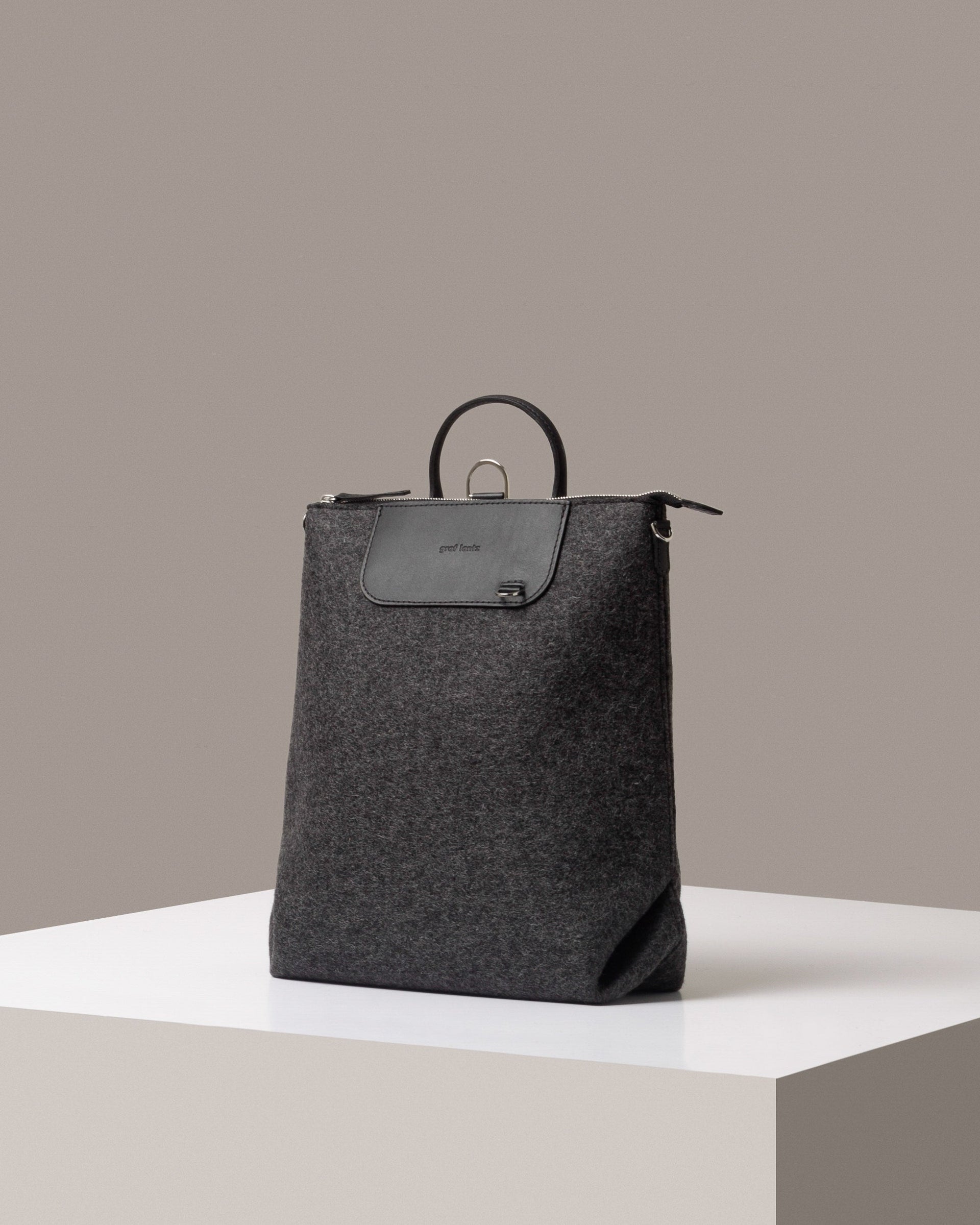 A stylish Bedford Merino Wool Felt Backpack in dark gray, displayed in a three-quarter view on a white base