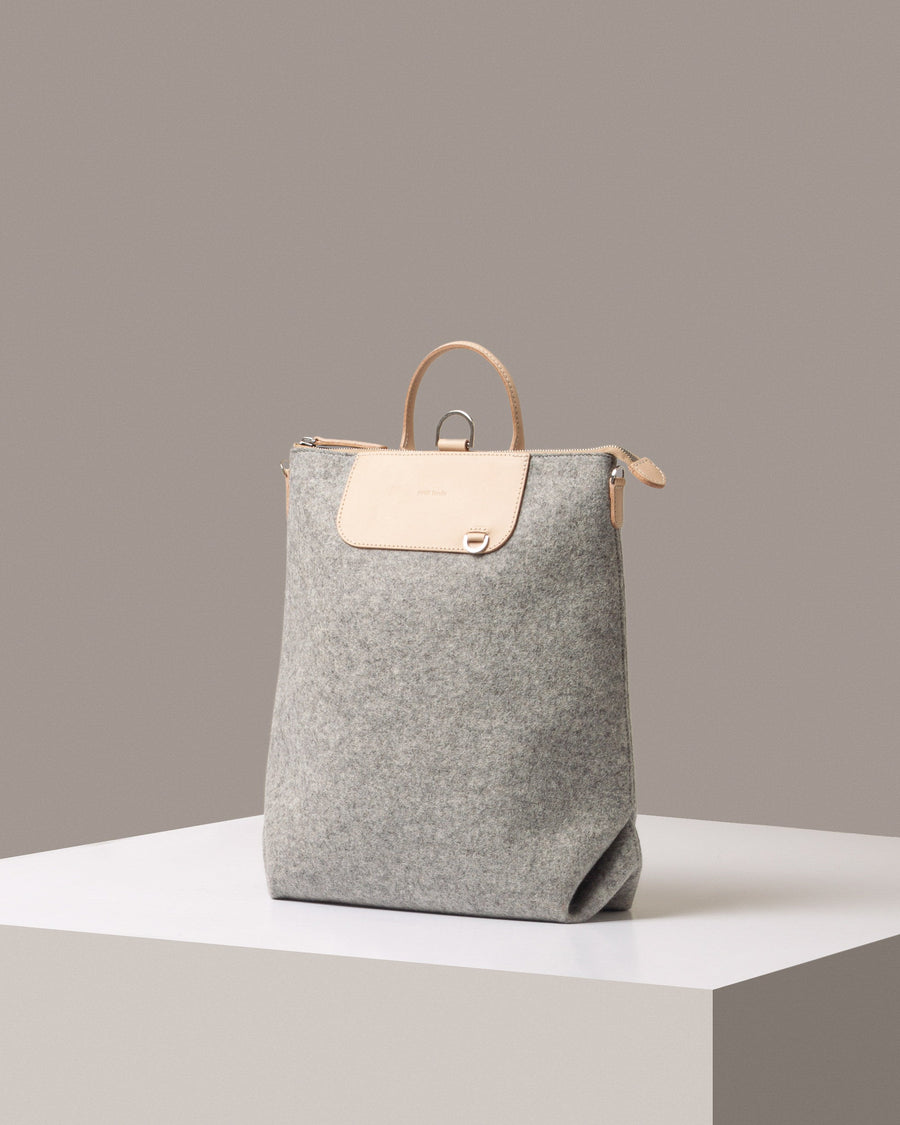 A stylish Bedford Merino Wool Felt Backpack in gray with beige leather accents, displayed in a three-quarter view on a white base