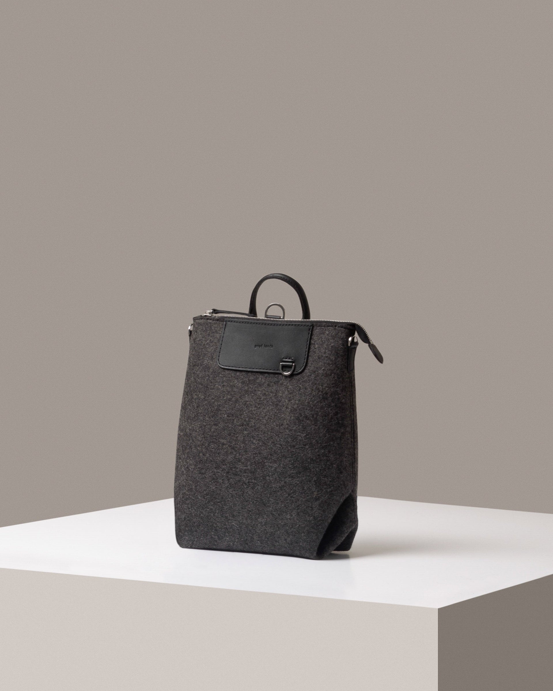 A Bedford Merino Wool Felt Midi Backpack in dark gray, displayed in a three-quarter view on a white base