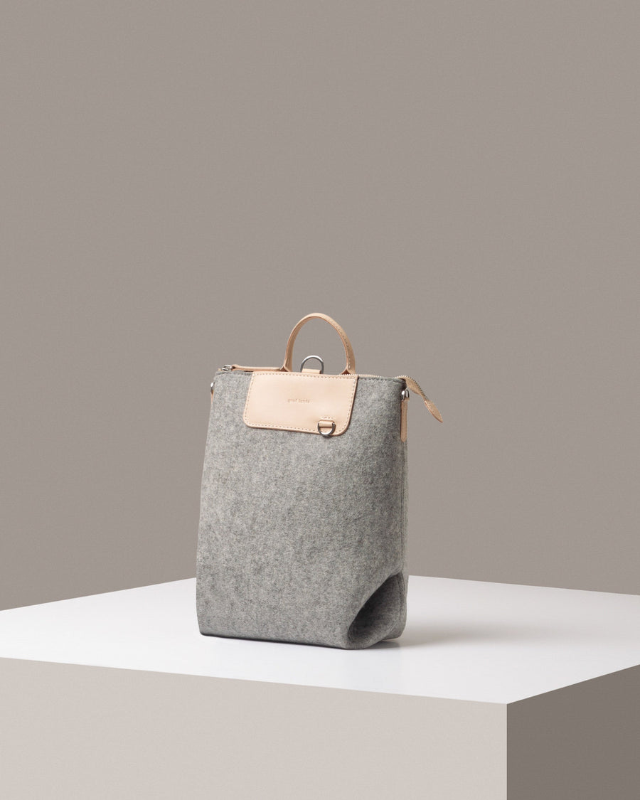 A stylish Bedford Merino Wool Felt Midi Backpack in light gray, displayed in a three-quarter view on a white base