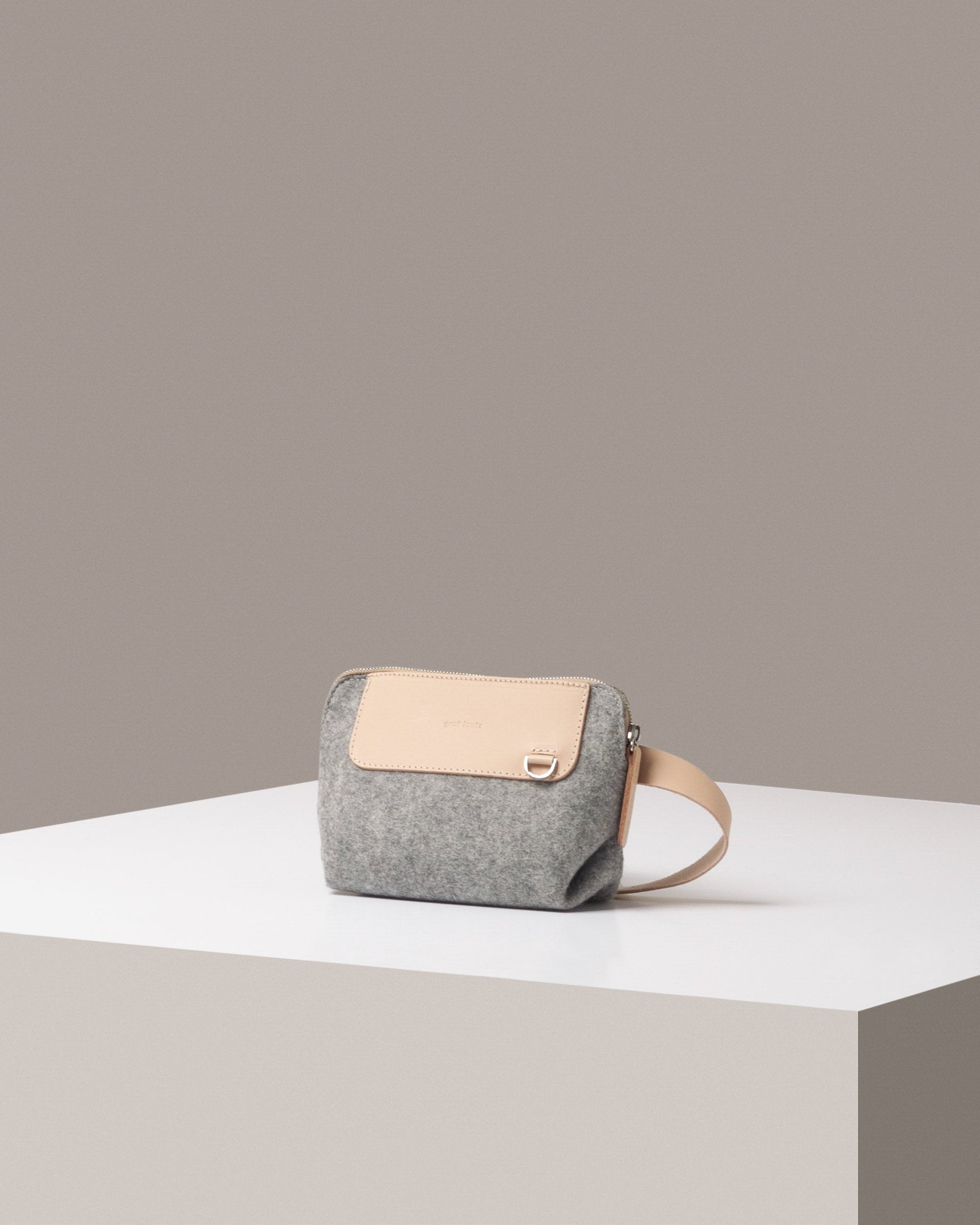 A stylish Bedford Merino Wool Felt Belt Bag in light gray with beige leather accents, displayed in a three-quarter view on a white base