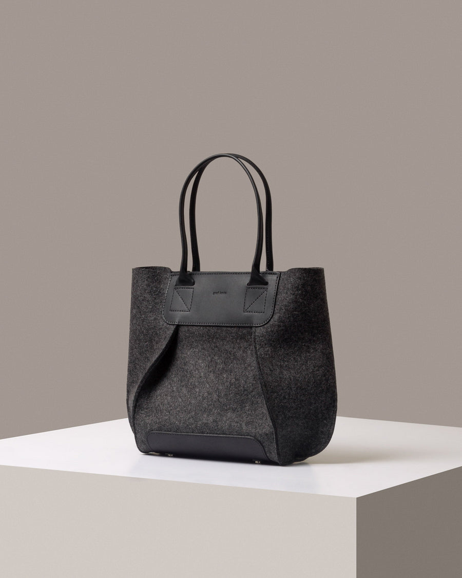 Mid-sized tote bag Frankie Merino Wool Felt Midi in dark gray with black leather handles, displayed in a three-quarter view on a white base