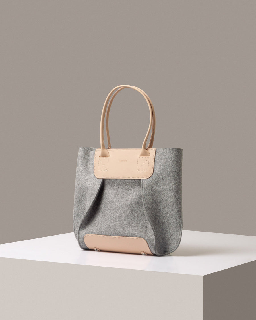 Mid-sized tote bag Frankie Merino Wool Felt Midi in gray with beige-colored leather handles, displayed in a three-quarter view on a white base