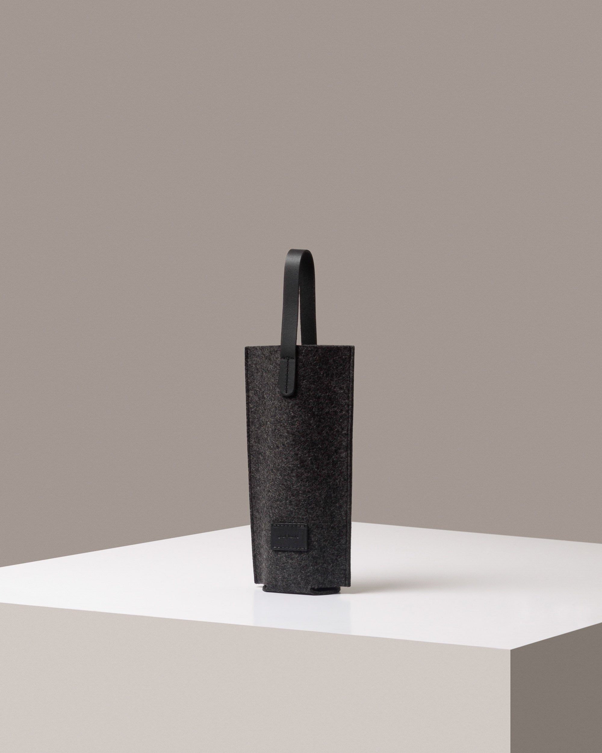 A stylish Hana Merino Wool Bottle Bag in dark gray, displayed in a three-quarter view on a white base