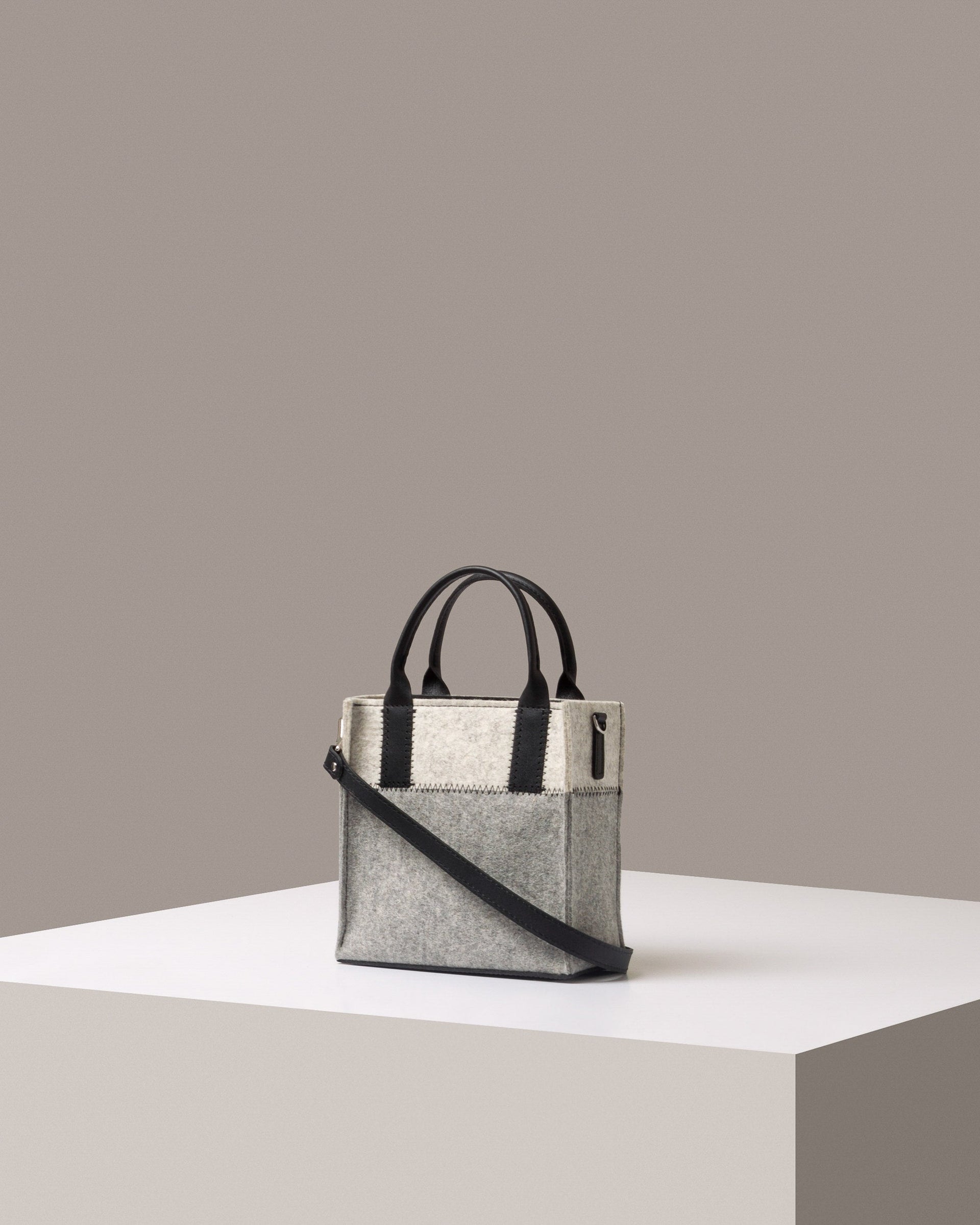 A Jaunt Mini Merino Wool Felt Tote bag in white and grey, with black accents and shoulder strap, displayed in a three-quarter view on a white base