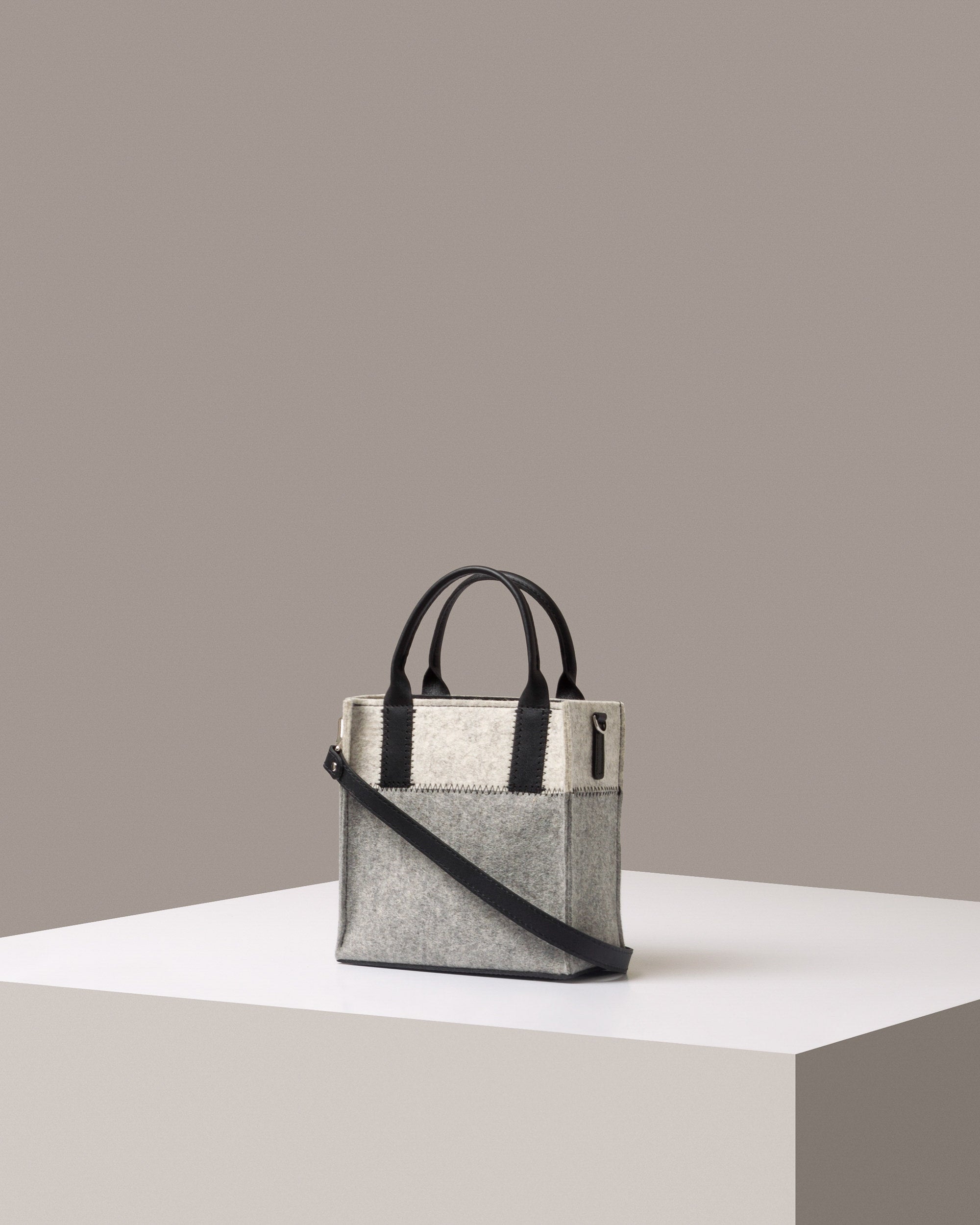 A Jaunt Mini Merino Wool Felt Tote bag in white and grey, with black accents and shoulder strap, displayed in a three-quarter view on a white base