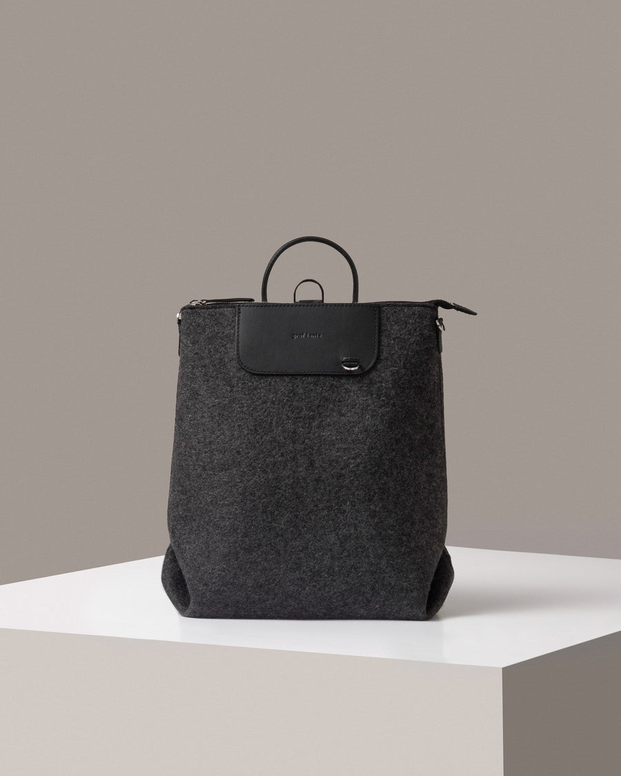 A Bedford Merino Wool Felt Backpack in dark gray standing on a white base, front view