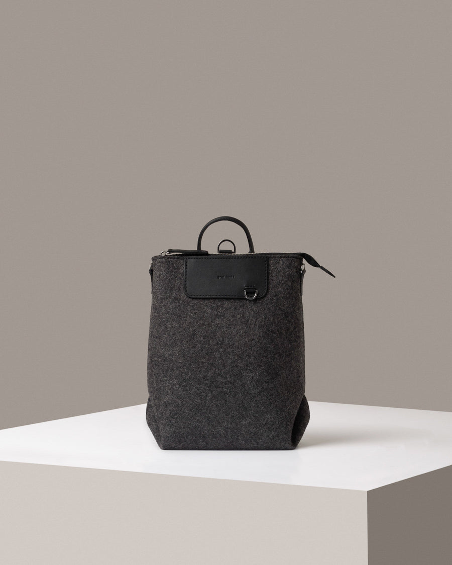 A Bedford Merino Wool Felt Midi Backpack in dark grey standing on a white base, front view