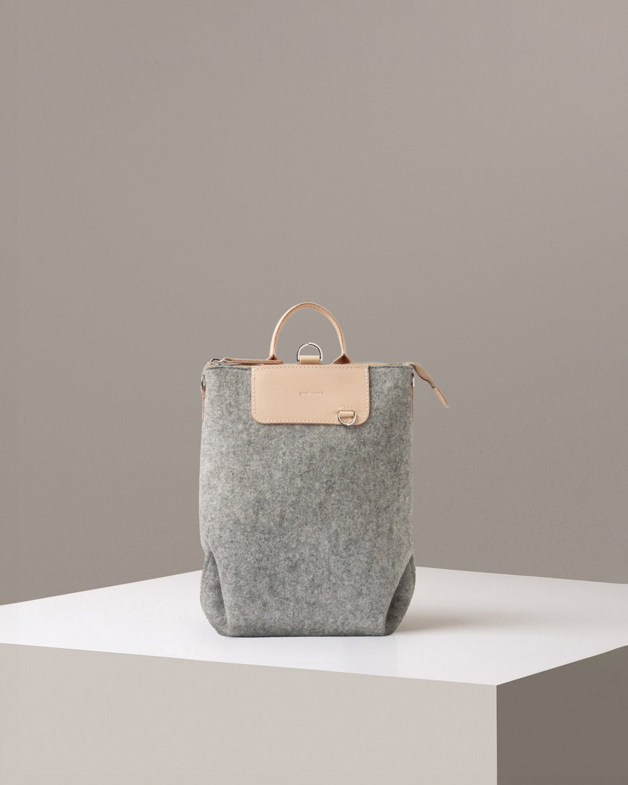 A Bedford Merino Wool Felt Midi Backpack in light grey standing on a white base, front view