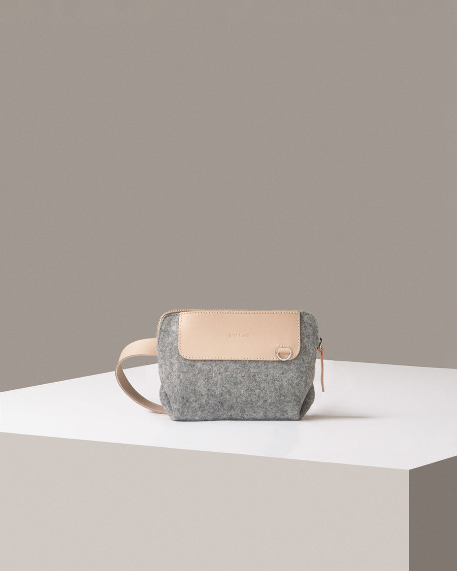A Bedford Merino Wool Felt Belt Bag in light grey standing on a white base, front view