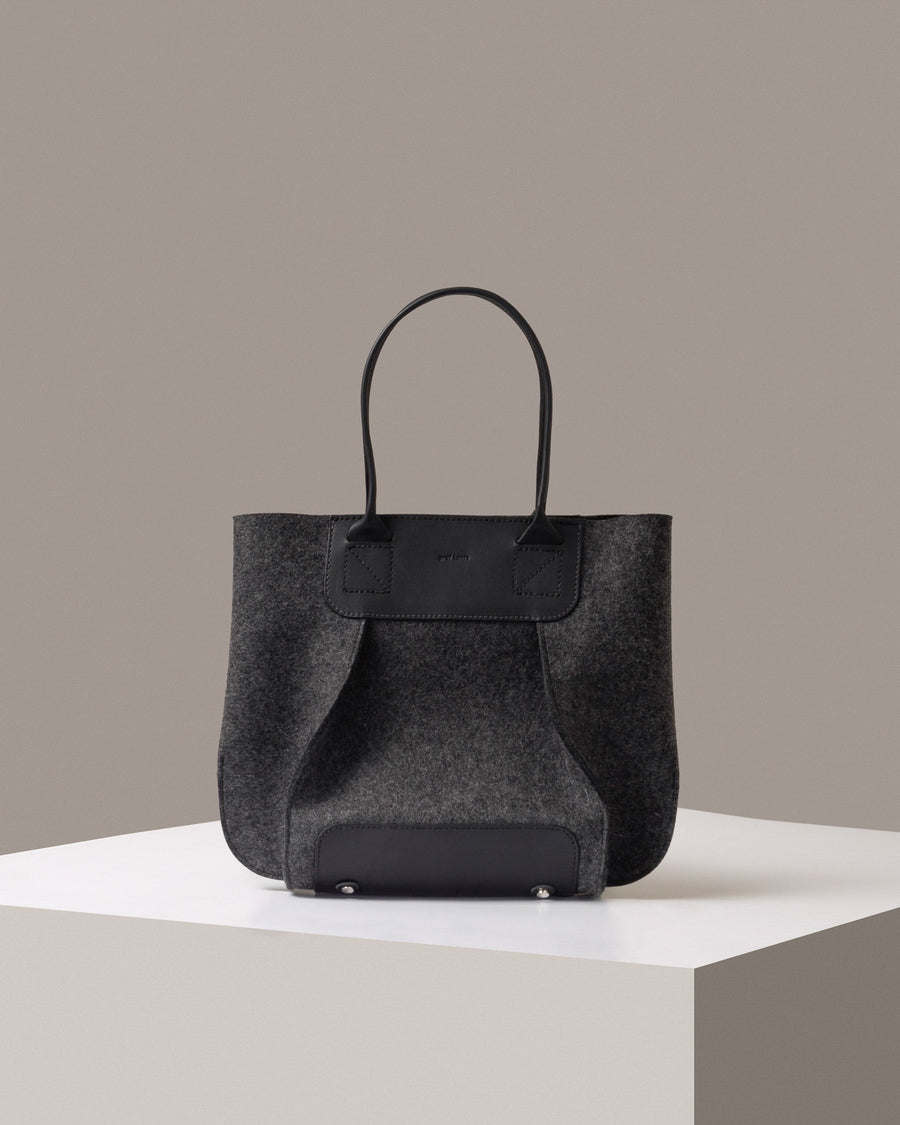 A Frankie Merino Wool Felt Midi mid-sized tote bag in dark grey standing on a white base, front view