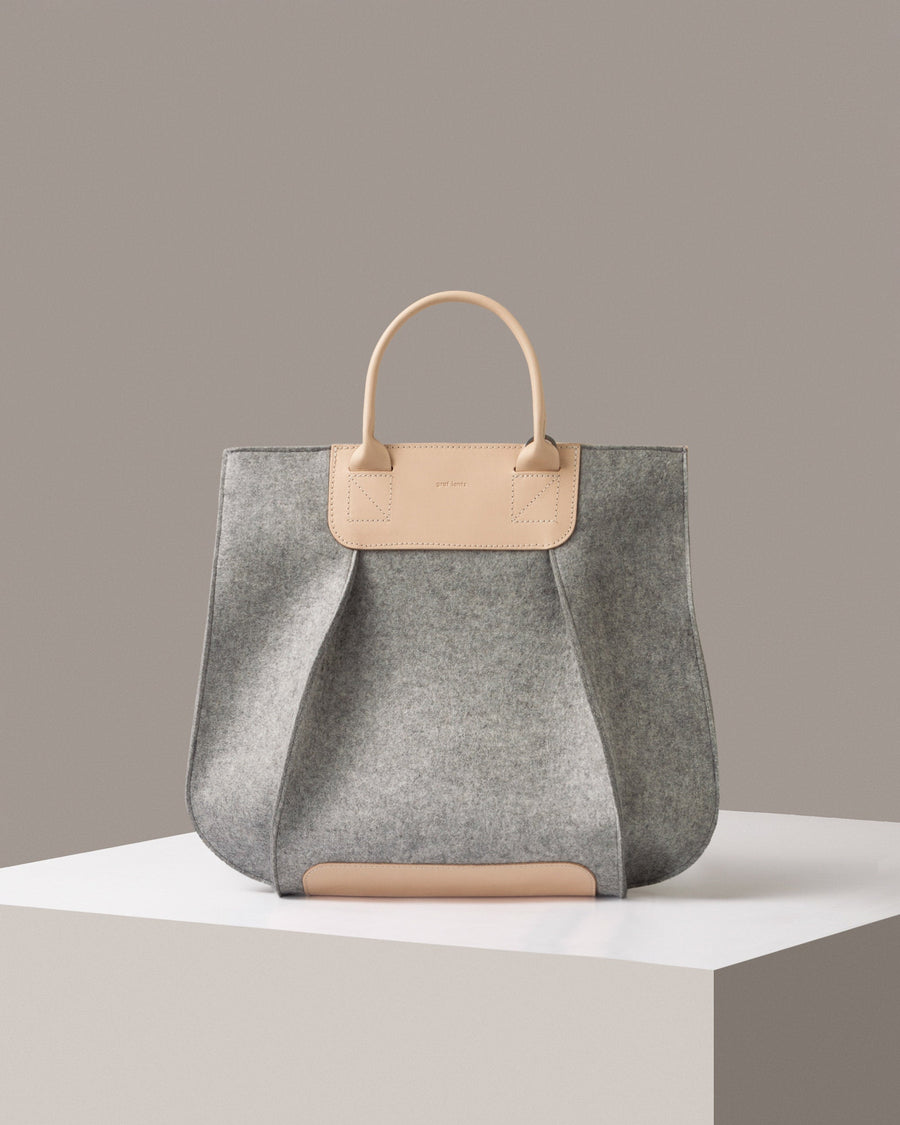 A grey Frankie Merino Wool Felt Tote bag standing on a white base, front view