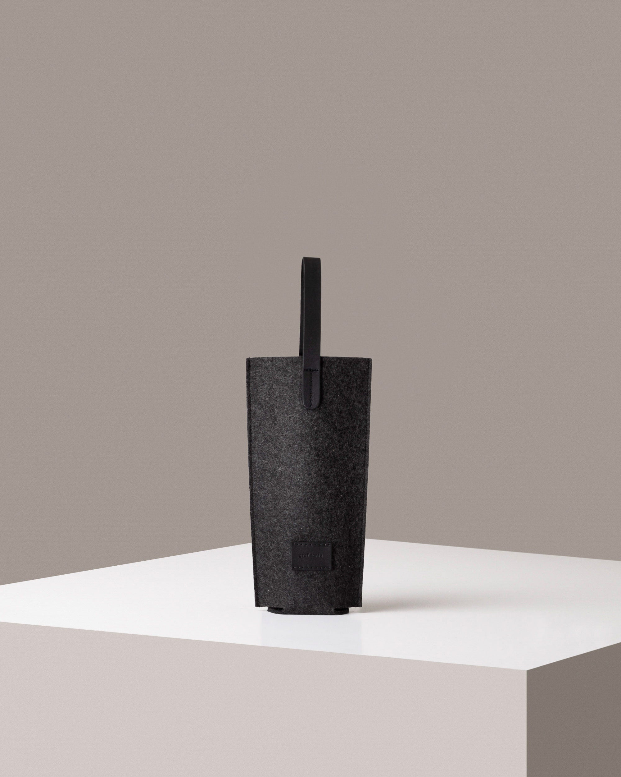 A Hana Merino Wool Bottle Bag dark grey standing on a white base, front view