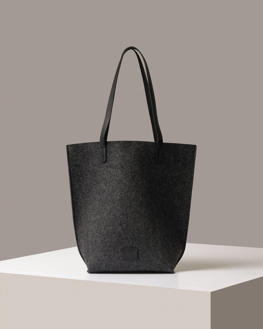 A Hana Merino Wool Felt Tote bag in dark gray standing on a white base, front view