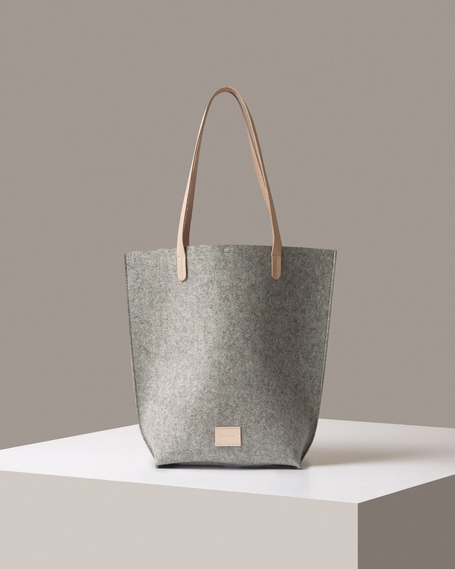 A Hana Merino Wool Felt Tote bag in gray standig on a white base, front view