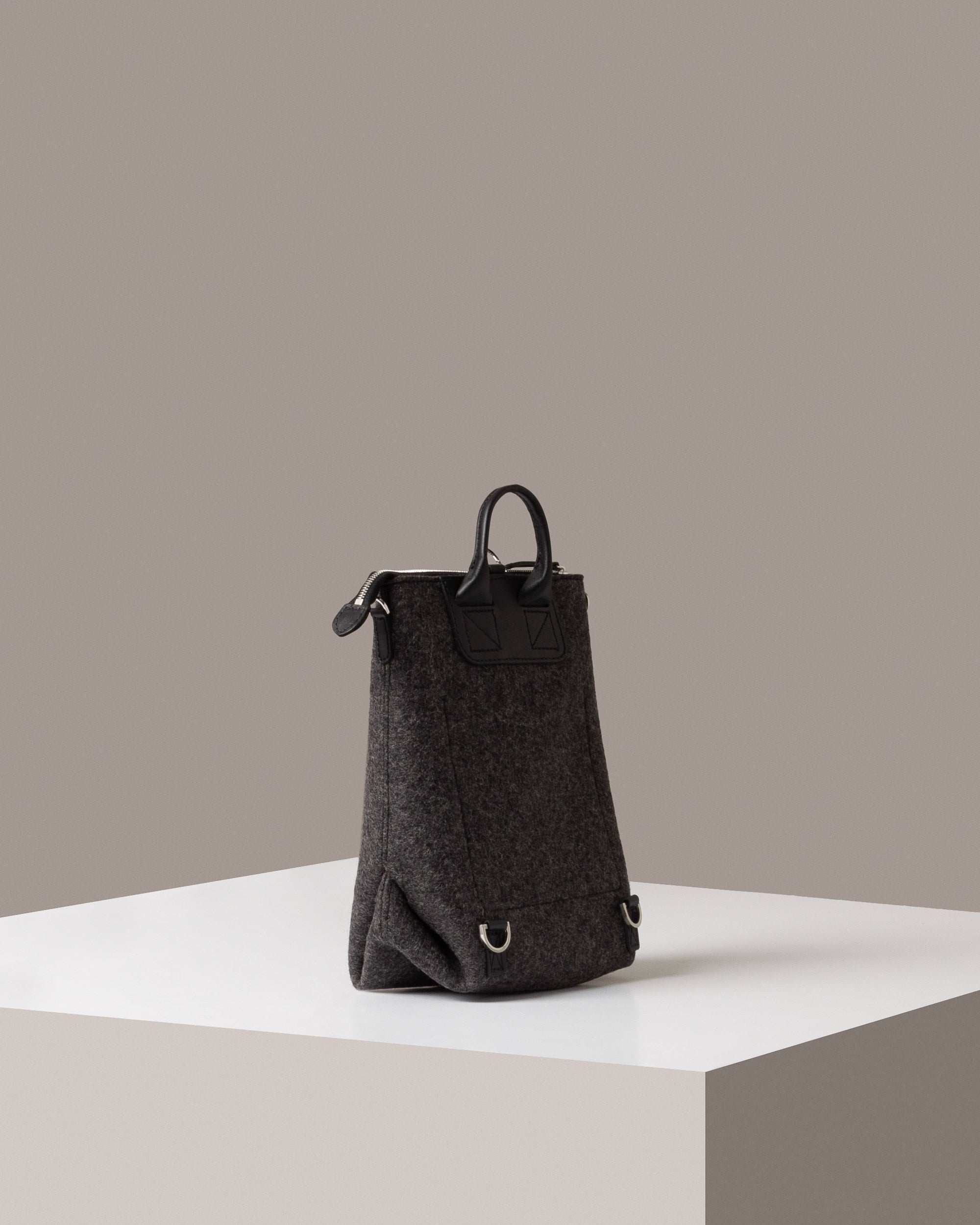 A dark grey Bedford Merino Wool Felt Midi Backpack on a white base displayed in a side-view
