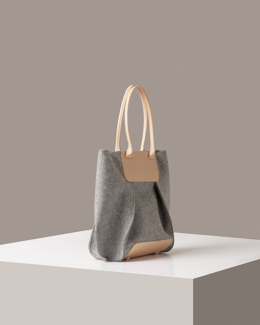 A light grey Frankie Merino Wool Felt Midi mid-sized tote bag on a white base displayed in a side-view
