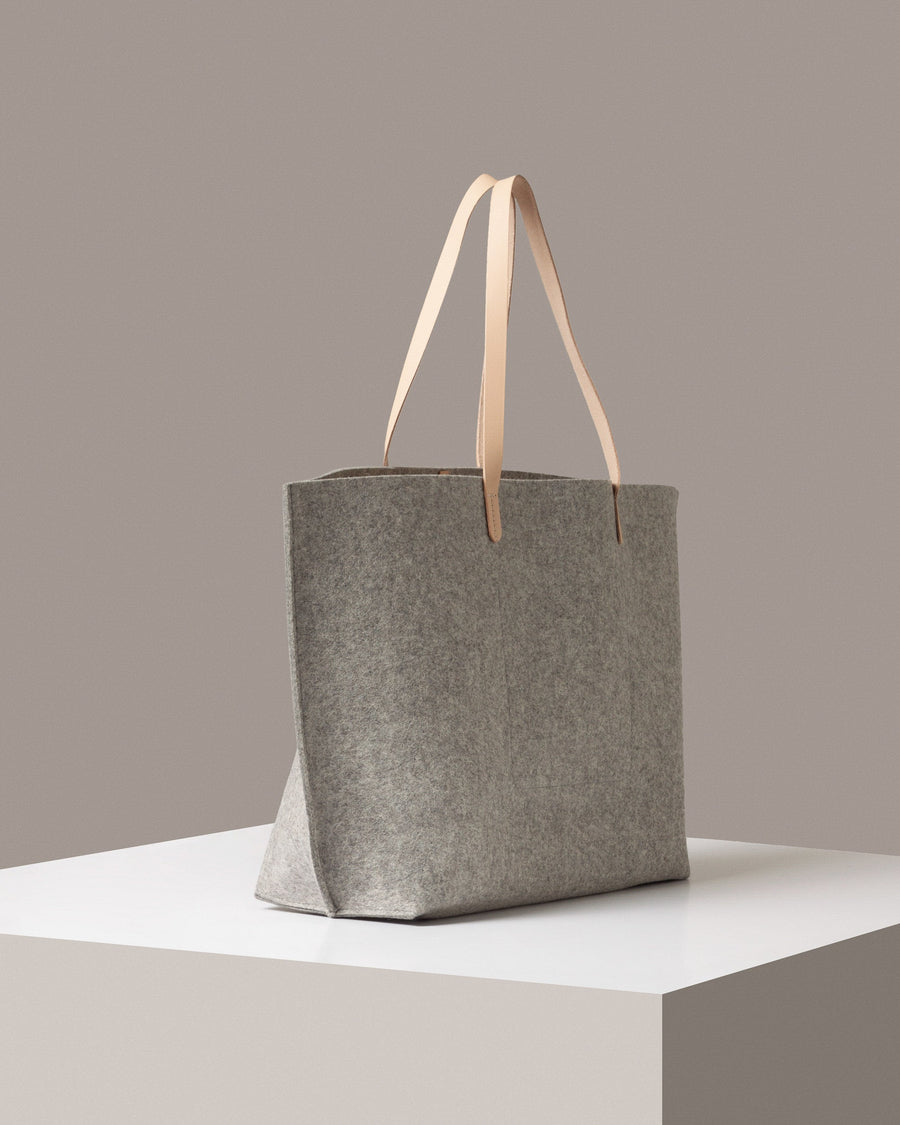 A Hana Merino Wool Felt Boat Bag in gray and beige colors on a white base displayed in a side-view
