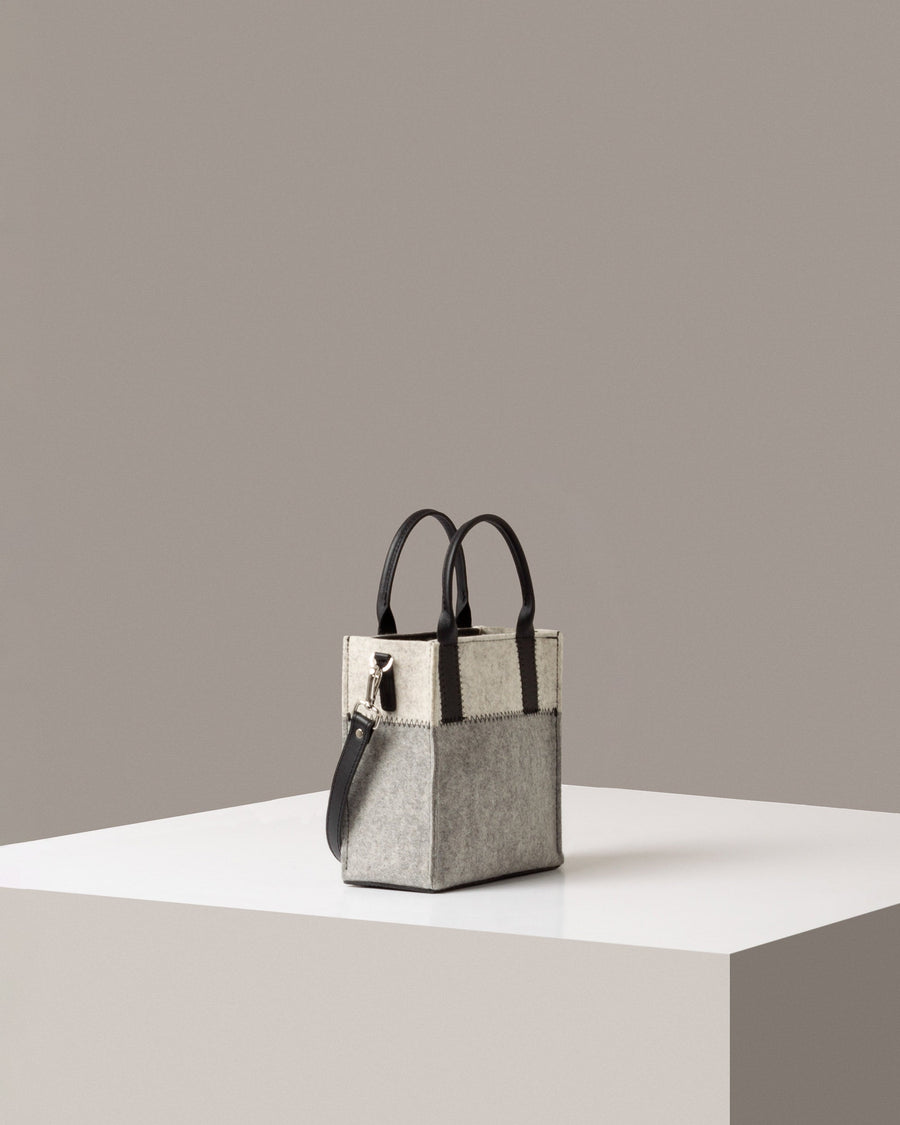 A timeless crossbody bag in gray and white on a white base displayed in a side-view

