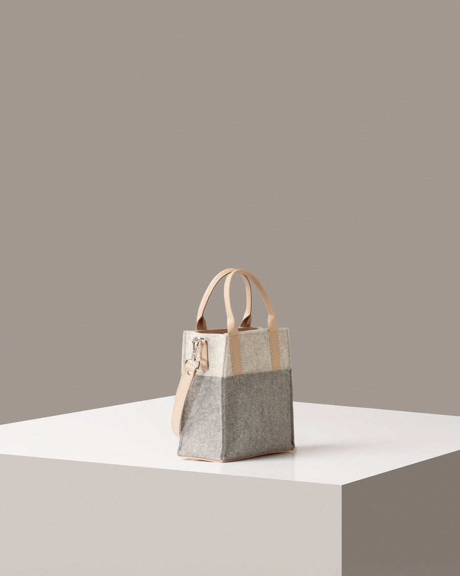 A Jaunt Mini Merino Wool Felt Crossbody bag in white, gray, and beige colors on a white base displayed in a side-view
