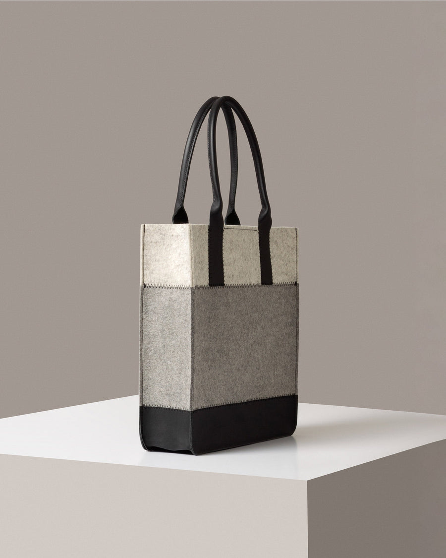 A Jaunt Merino Wool Felt Tote in gray, white, and black colors on a white base displayed in a side-view
