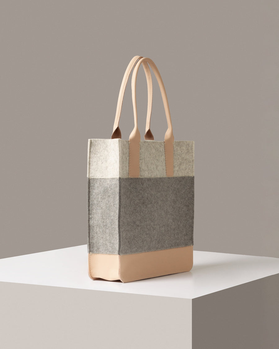 A Jaunt Merino Wool Felt Tote in white, gray, and beige colors on a white base displayed in a side-view
