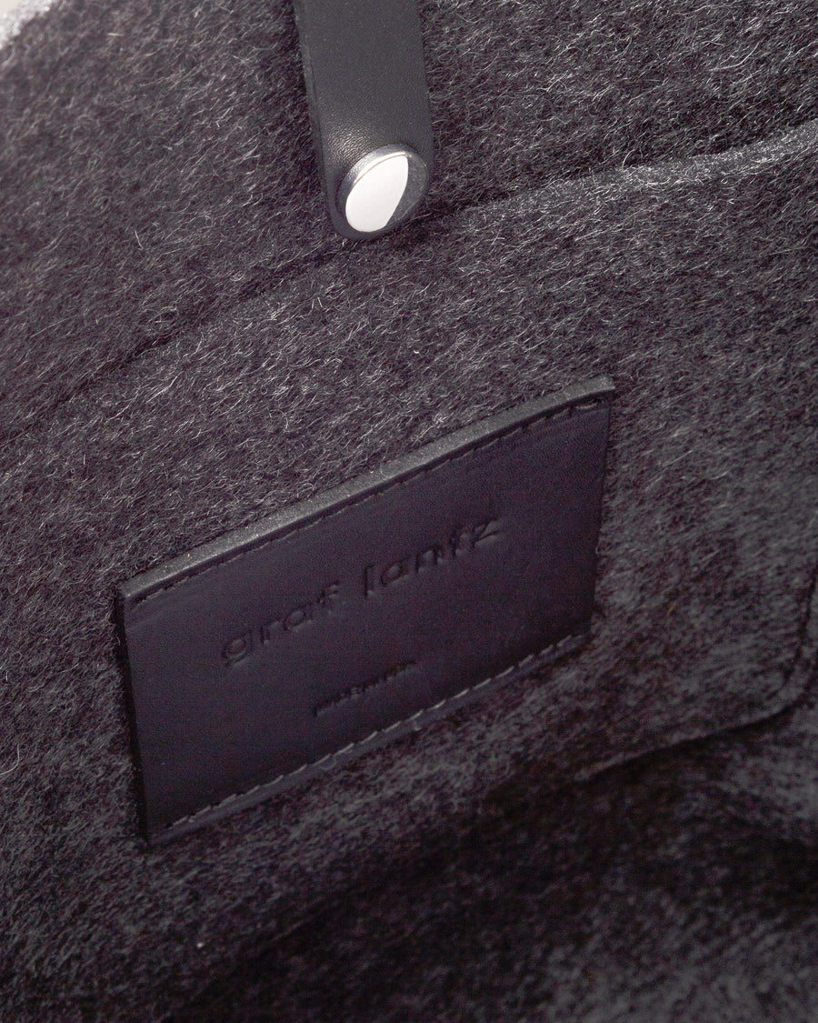 Interior view of a dark grey Hana Merino Wool Felt Boat Bag featuring a felt pocket and a snap closure, highlighted in detail