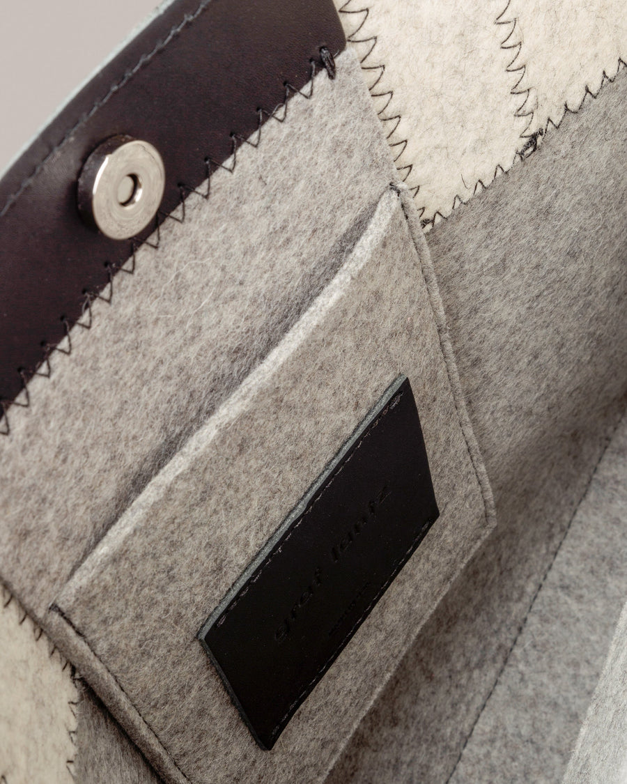 Interior view of a gray Jaunt Midi Merino Wool Felt Tote bag featuring a felt pocket, black leather trim, and a magnetic snap closure, highlighted in detail