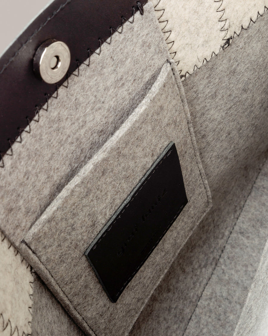 Interior view of a grey Jaunt Merino Wool Felt Tote bag featuring a felt pocket, black leather trim, and a magnetic snap closure, highlighted in detail