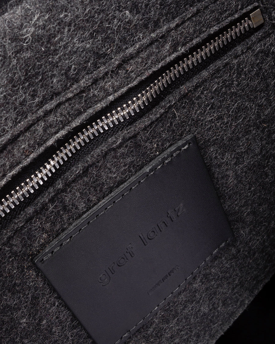 Interior view of dark grey Bedford Merino Wool Felt Backpack featuring a zippered felt pocket, black leather trim, and nickel hardware, highlighted in detail
