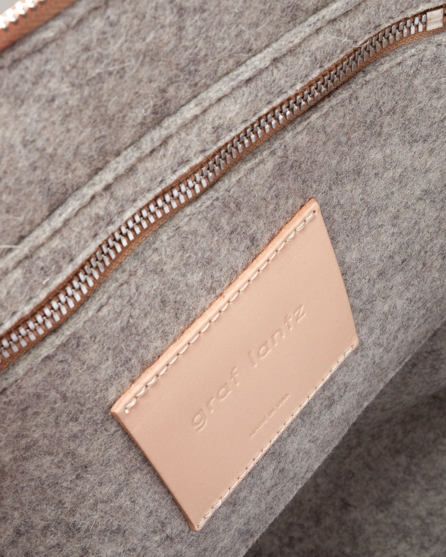 Interior view of a grey Bedford Merino Wool Felt Backpack featuring a zippered felt pocket, beige leather trim, and nickel hardware, highlighted in detail