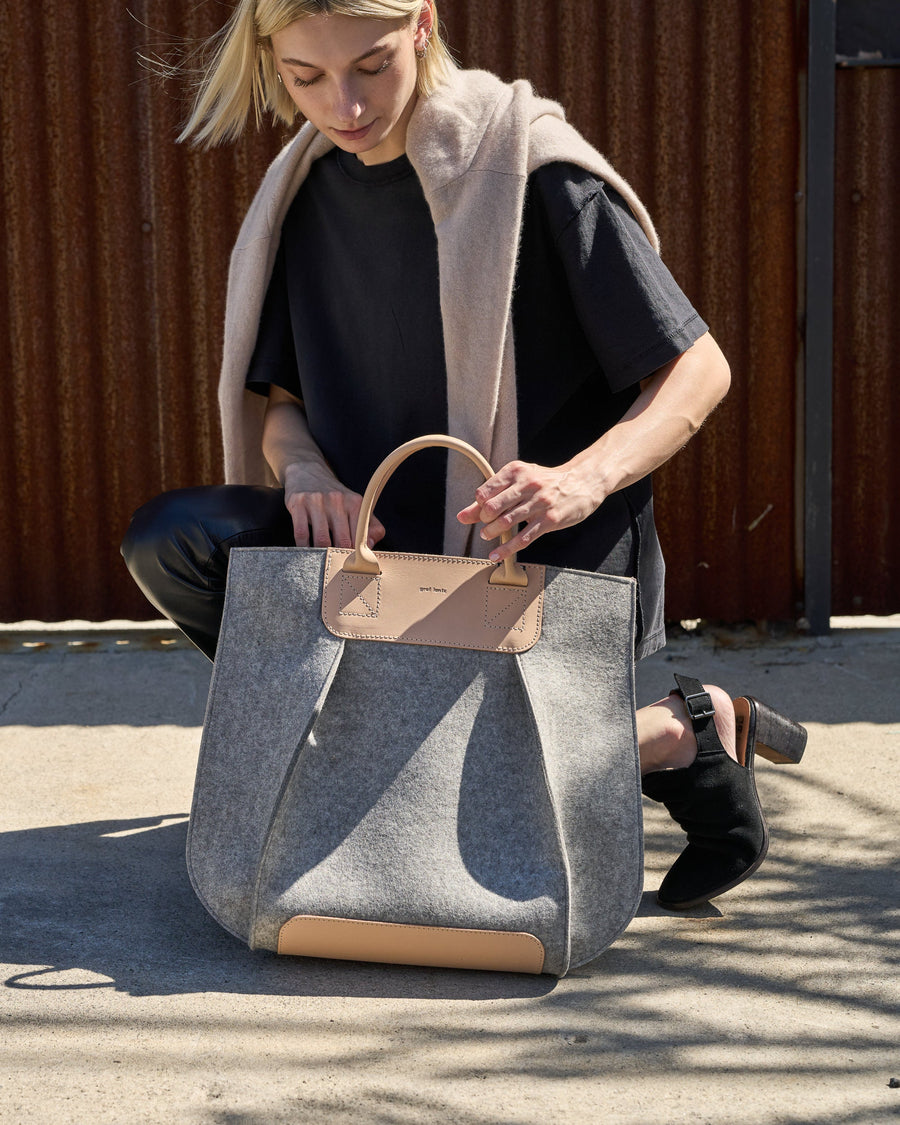 Stylish woman squatting with a granite-colored Frankie Merino Wool Felt Tote bag, demonstrating the bag's design and functionality
