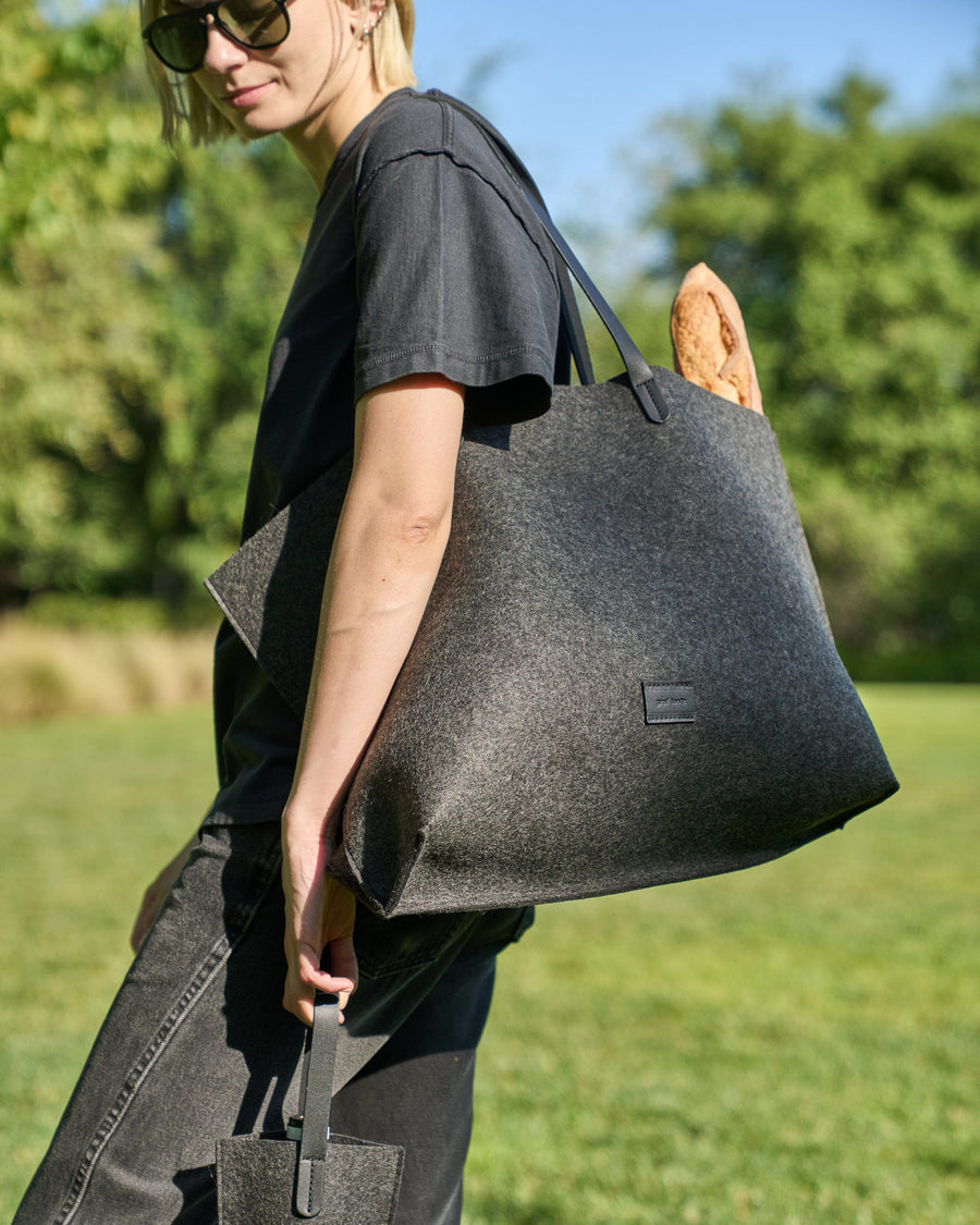 A Hana Merino Wool Felt Boat Bag carried by a woman over her shoulder, showcasing its dark grey and black colors
