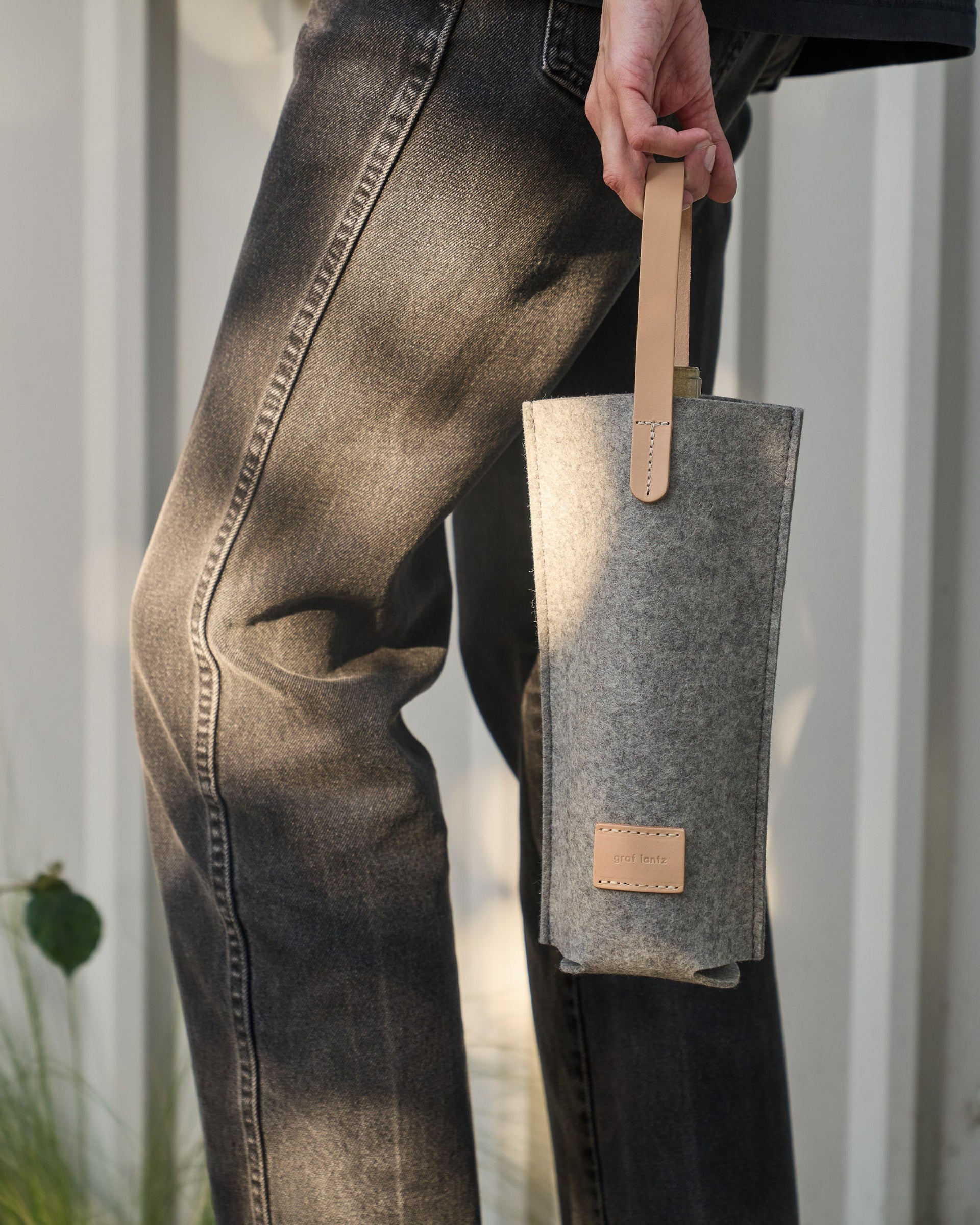 A Hana Merino Wool Bottle Bag carried by a woman, showcasing its light grey and beige colors