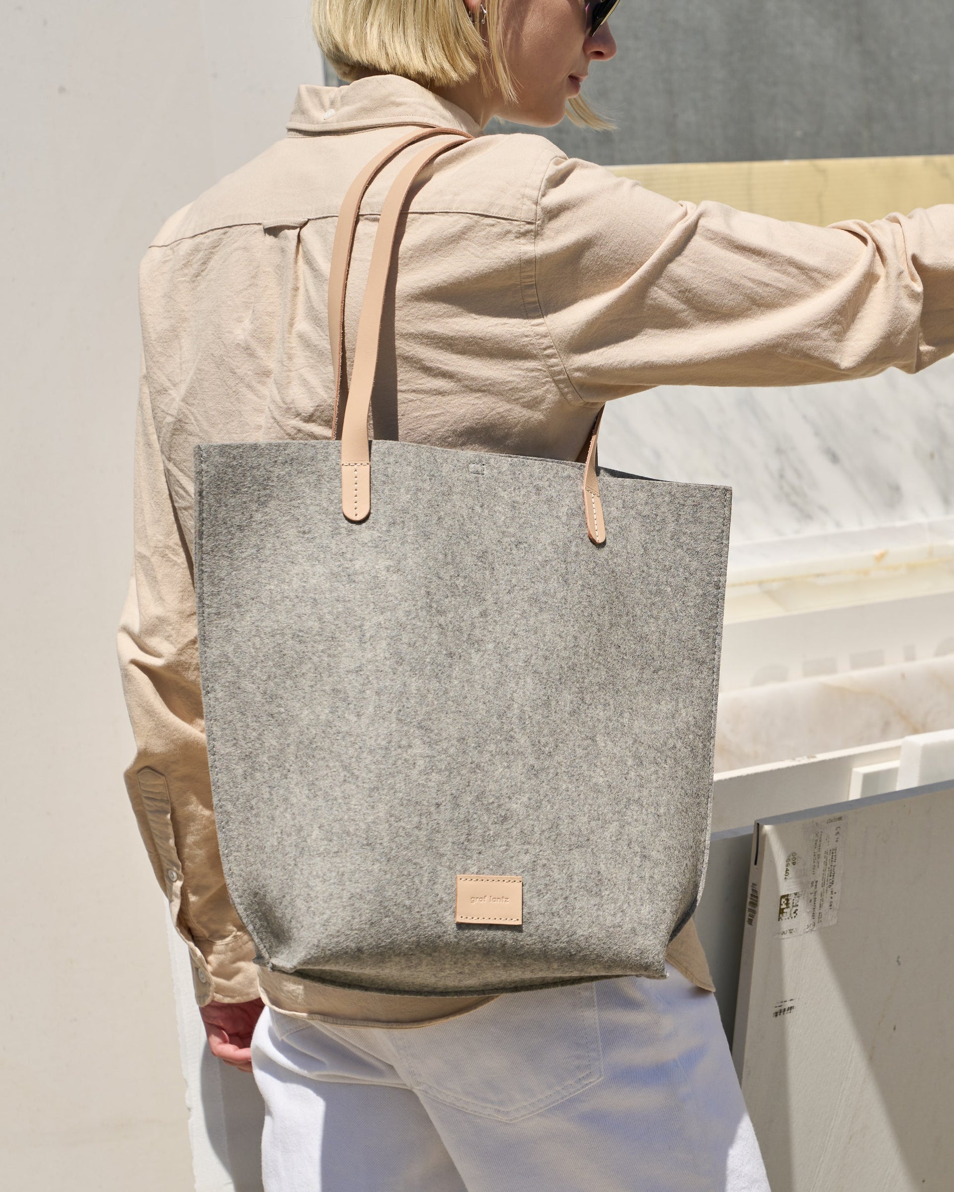 A granite-colored Hana Merino Wool Felt Tote carried by a woman over her shoulder, showcasing its grey and beige colors