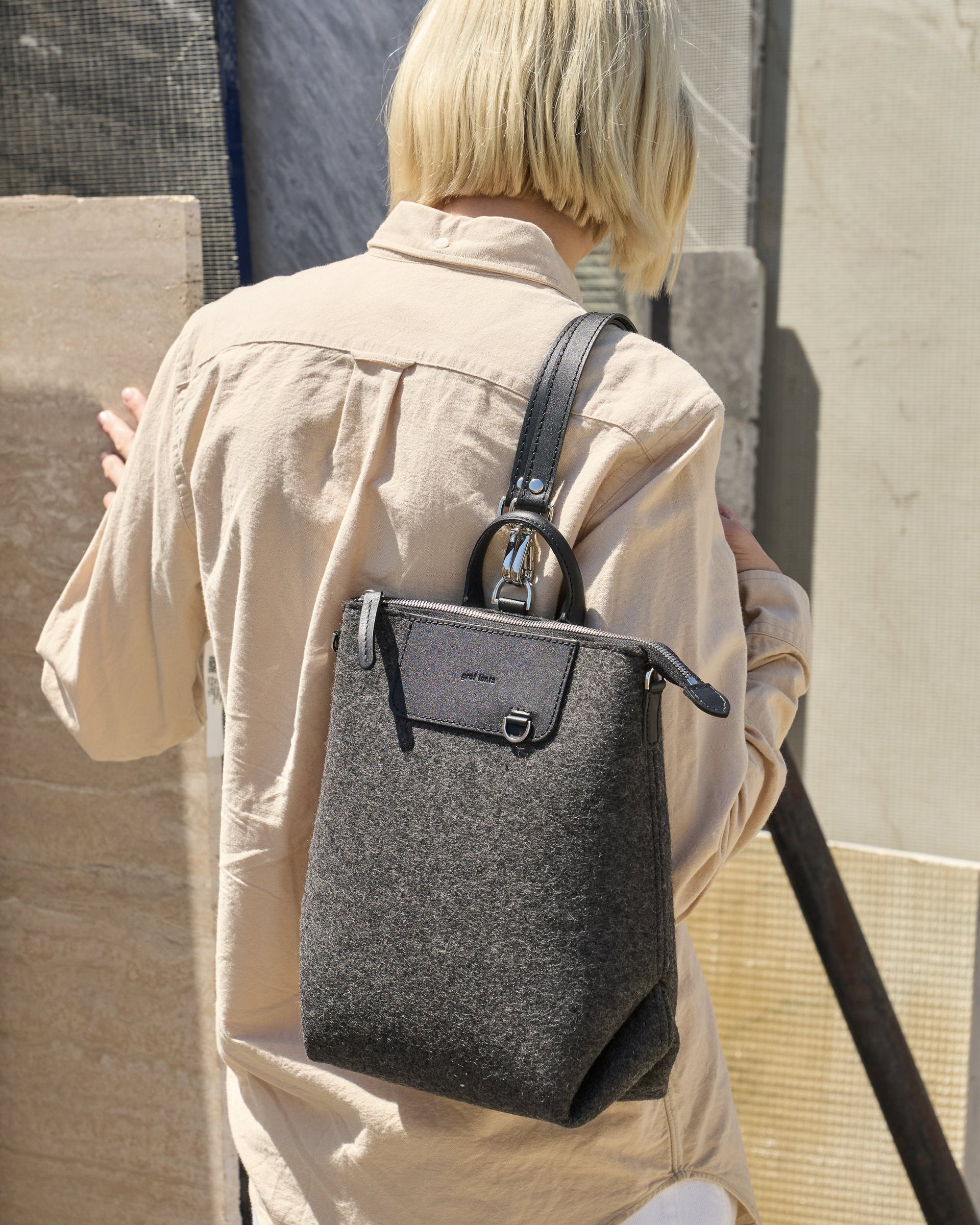 A Bedford Merino Wool Felt Midi Backpack carried by a woman over her shoulder, showcasing its dark grey and black colors