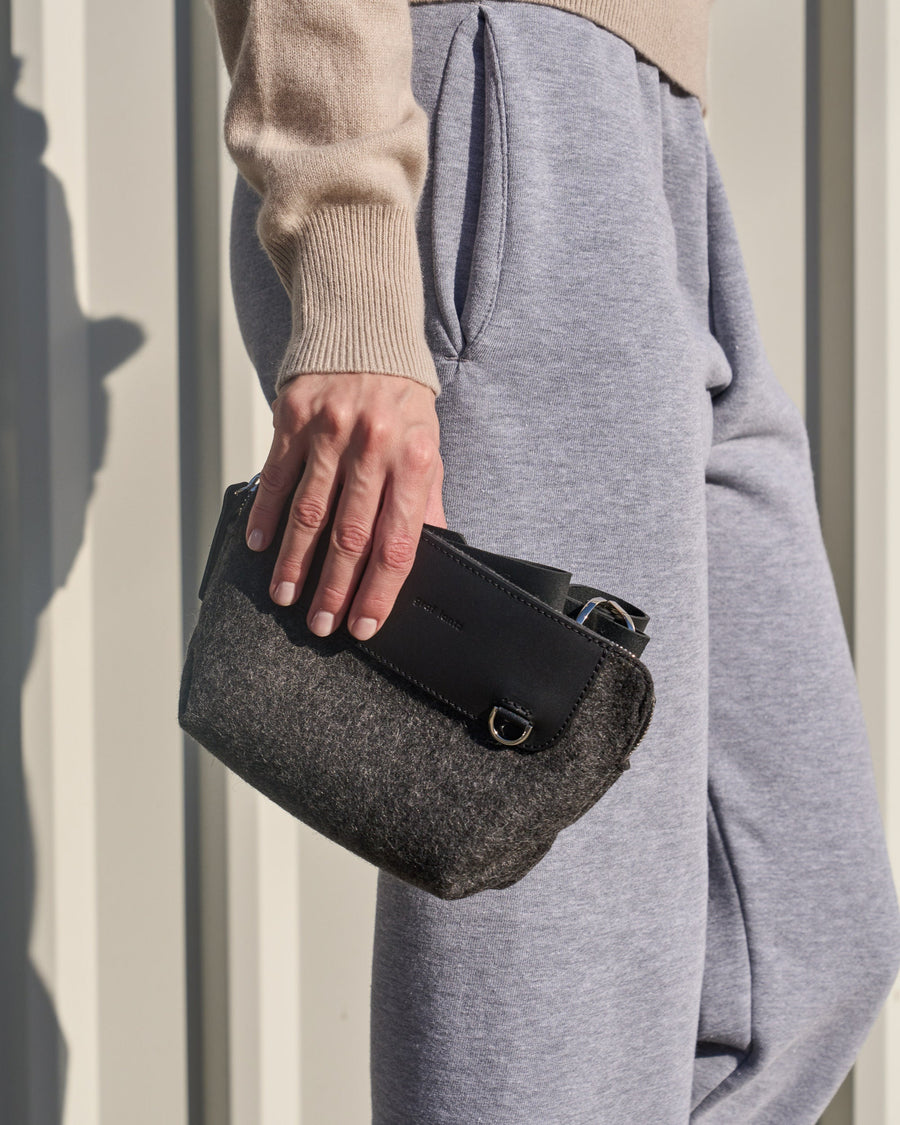 A charcoal-colored Bedford Merino Wool Felt Belt Bag carried in a woman's hand, showcasing its sleek design