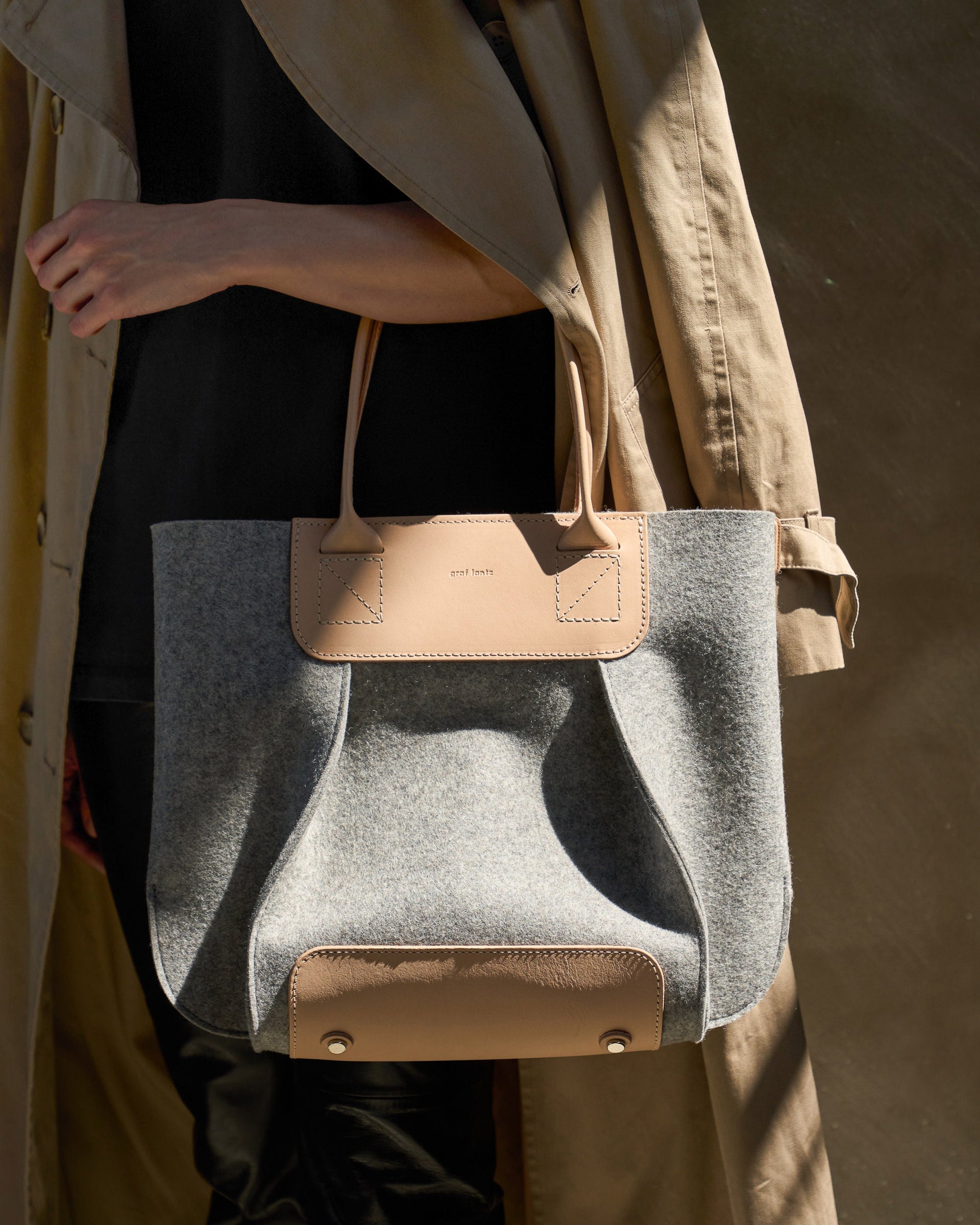 A woman carries a Frankie Merino Wool Felt Midi tote over her arm while walking, showcasing its size and chic design