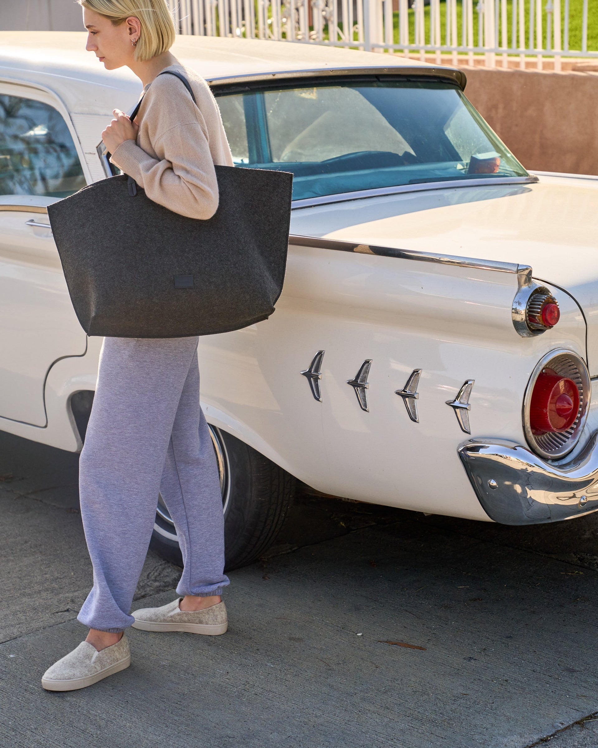A woman carries a Hana Merino Wool Felt Boat Bag over her shoulder standing in front of a classic car